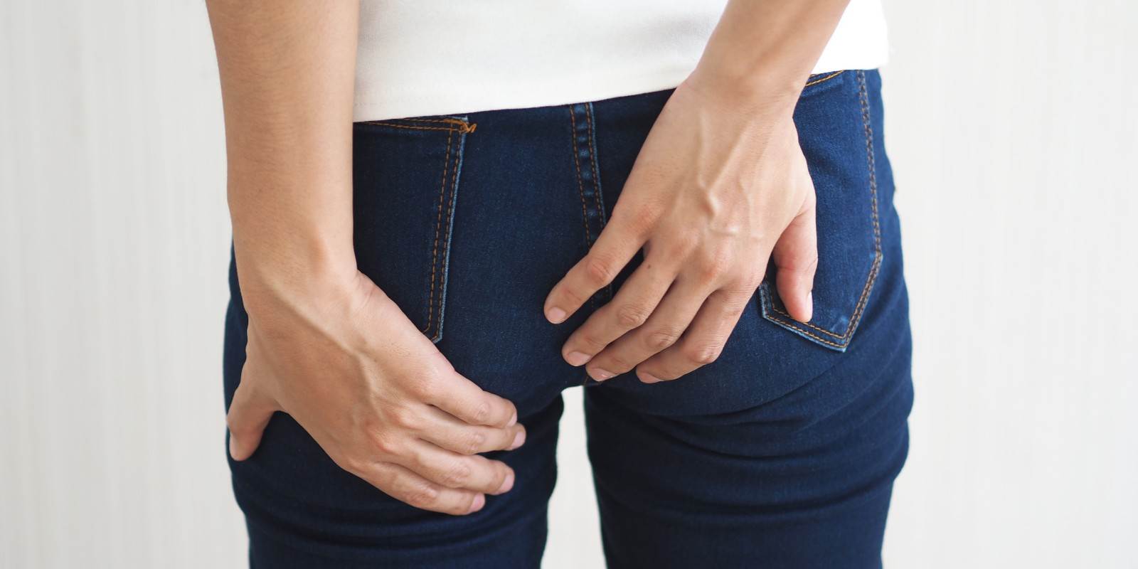 Eine Frau in blauen Jeans greift sich zum Thema Hämorrhoiden ans Gesäss