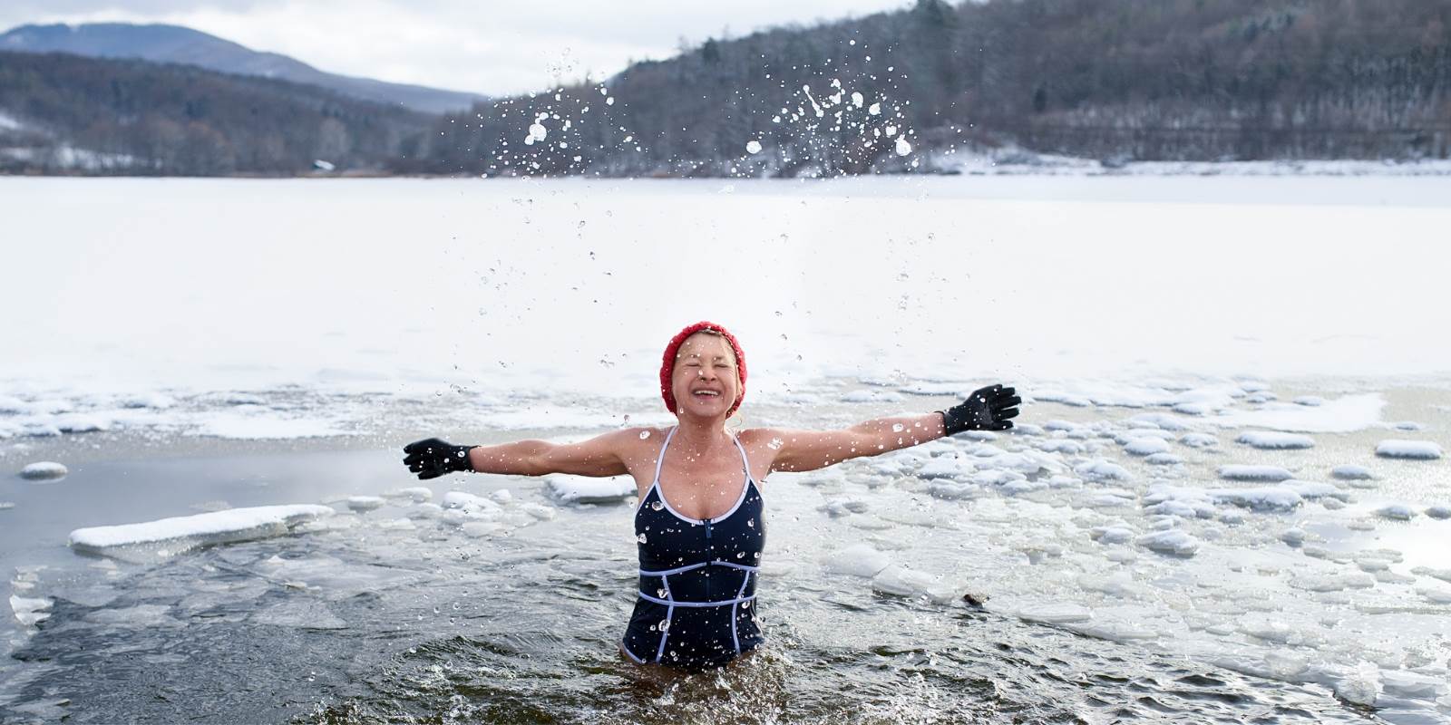 ältere Frau im Winter im See mit Kappe und Hanschuhen